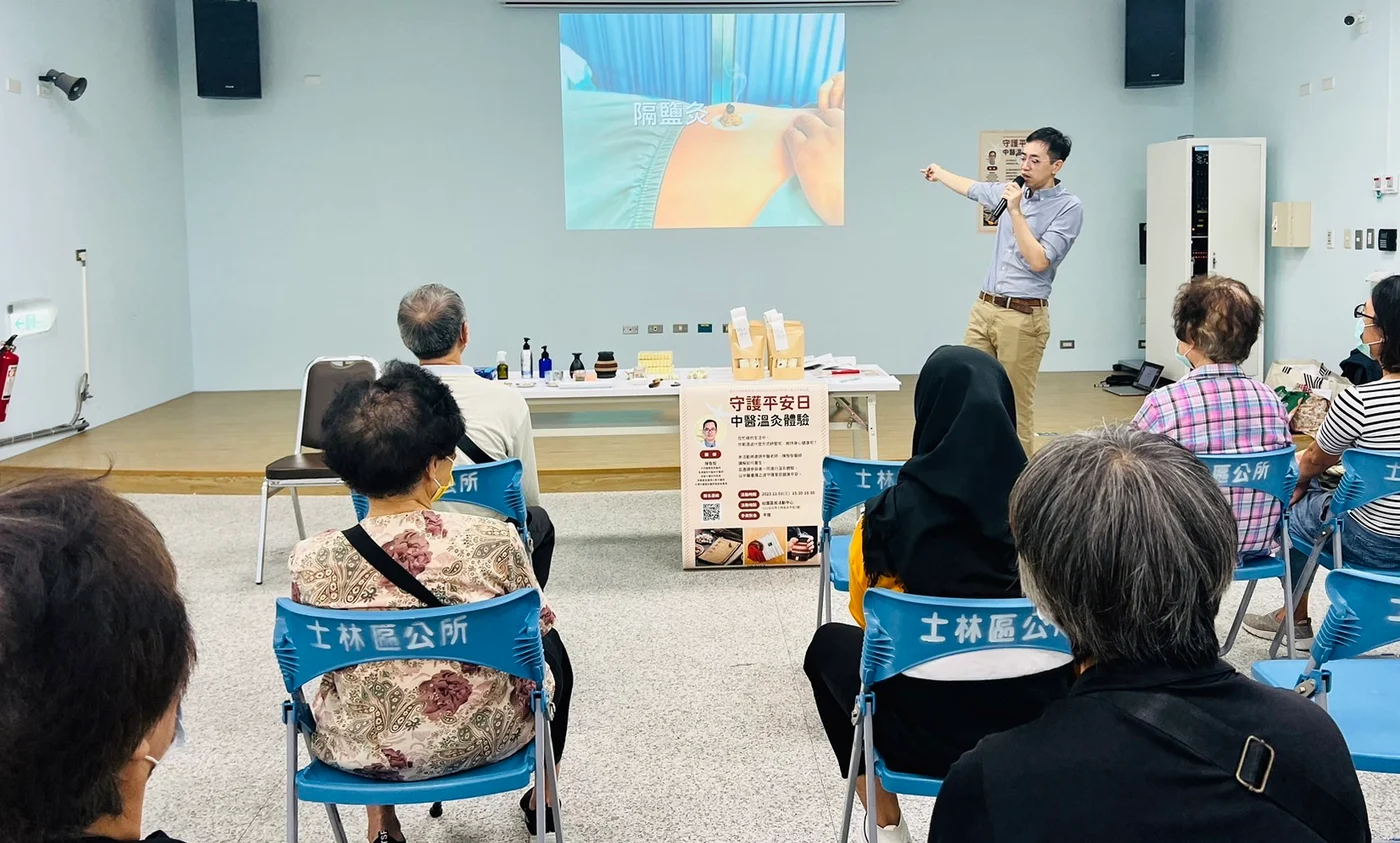 陳敬智中醫師在士林區公所的中醫溫灸講座上指著投影幕解說,台下坐著參與的民眾